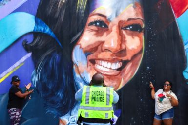 A Chicago police officer photographs people posing before a mural of US Vice President Kamala Harris outside the United Center ahead of the Democratic National Convention